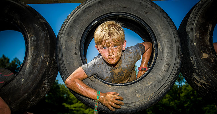Splat: Muddy boy peeking out from a tire.